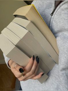 a woman with black nail polish holding an open book in her hands and looking at the camera