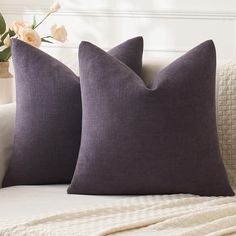 two pillows sitting on top of a bed next to a vase with flowers in it