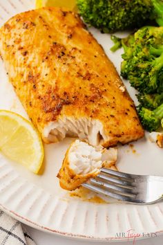 a piece of fish on a plate with broccoli and lemon wedges next to it