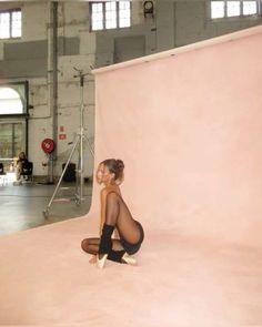 a woman sitting on the ground in front of a pink wall