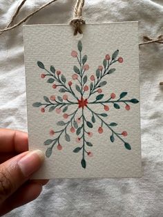 a hand holding a piece of paper with watercolor paint on it that has a snowflake design