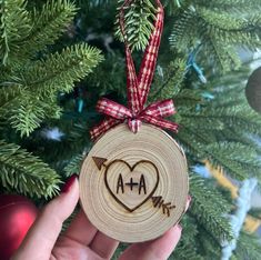 a hand holding a wooden ornament with an arrow and heart on it in front of a christmas tree