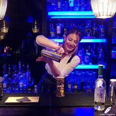 a woman is making a drink at a bar with liquor bottles behind her and on the counter