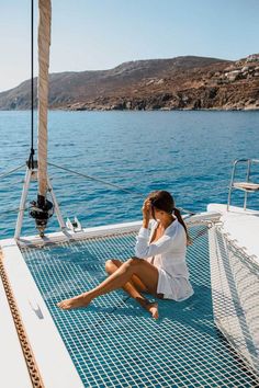 a woman sitting on the deck of a sailboat while talking on her cell phone