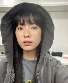 a woman with long black hair wearing a gray hoodie and looking at the camera