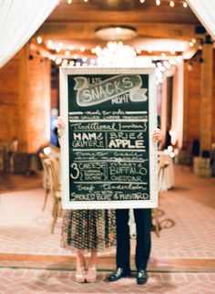 a man and woman holding up a chalkboard sign in front of a restaurant entrance