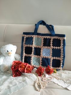 a crocheted bag, flowers and a teddy bear are sitting on a bed