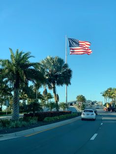 an american flag flying in the air over a street with palm trees and cars driving down it