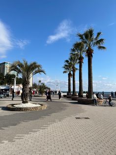 palm trees and people walking on the sidewalk in front of some buildings with blue skies