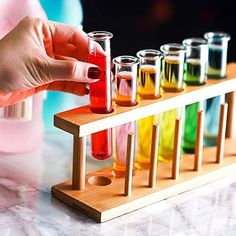 a person holding a test tube filled with colored liquid in front of a row of test tubes