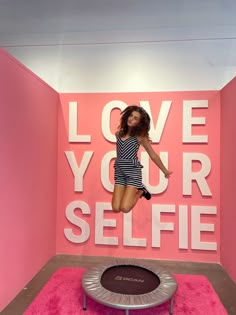 a woman jumping on a trampoline in front of a love your selfie sign