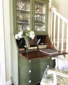 a green cabinet with flowers and books on it next to a stair case in a home