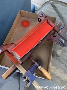 a red object sitting inside of a cardboard box on top of a metal flooring machine