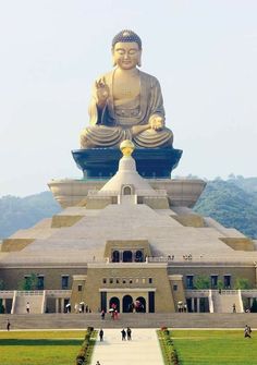 a large buddha statue sitting on top of a lush green field