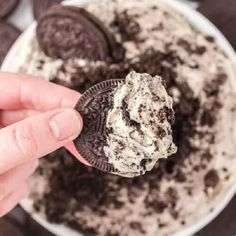 a hand holding an oreo cookie in front of a bowl of cookies and cream