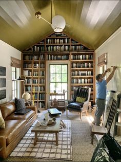 a man standing in the middle of a living room filled with furniture and bookshelves