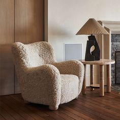 a living room with a chair, table and lamp on the hardwood floor in front of a fireplace