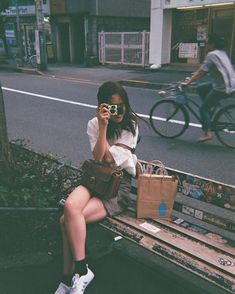 a woman is sitting on a bench talking on her cell phone and holding a purse