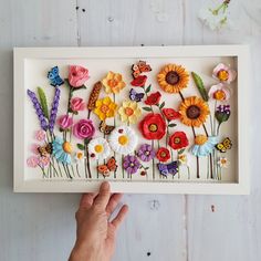 a person is holding up a shadow box with flowers in it and butterflies on the side