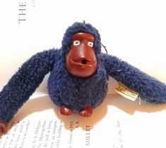 a blue stuffed gorilla sitting on top of an open book with a tag in it's ear