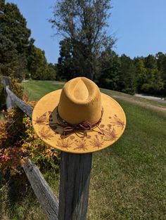 This tumeric yellow hand burnt wide brim fedora would make a perfect addition to any nature lover's wardrobe. The faux suede earthen yellow material burns a rich brown allowing the design to stand out. On the backside brim of the hat I hand burnt and shaded dandelion plants. On the front of the crown I burnt a single dandelion plant. I distressed the hat with stitch marks along the crown and brim of the hat. The design is original and completely free-handed. For a finishing touch I added a brown Yellow Curved Brim Fedora For Kentucky Derby, Yellow Fedora Hat For Fall, Yellow Western Hat With Curved Brim, Yellow Western Hat With Short Brim, Yellow Brimmed Fedora For Kentucky Derby, Yellow Fedora For Kentucky Derby, Yellow Fedora Sun Hat For Kentucky Derby, Adjustable Yellow Fedora For Kentucky Derby, Yellow Adjustable Fedora For Kentucky Derby