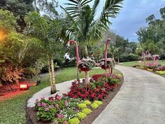 a pathway with flowers and palm trees in the middle of it, surrounded by greenery