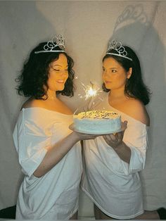 two women in white dresses holding a cake with sparklers on it and looking at each other