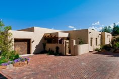 an adobe - style house is shown in the middle of a brick driveway with potted plants on either side