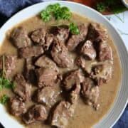 a white plate topped with meat and gravy on top of a blue table cloth