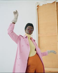 a woman in a pink coat and orange pants with her hands up to the side