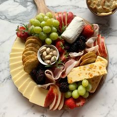 a platter filled with cheese, fruit and crackers on top of a marble counter