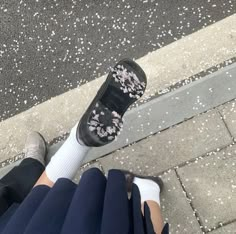 a person wearing black and white shoes standing next to a curb with flowers on it