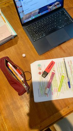 an open laptop computer sitting on top of a wooden desk next to a notebook and pencils