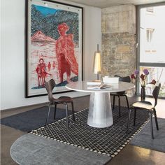 a dining room table and chairs in front of a large window with an art work on the wall