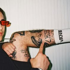 a man with tattoos on his arm giving the thumbs up sign while wearing red sunglasses