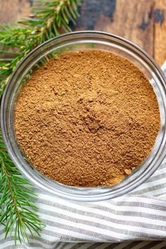 a glass bowl filled with cinnamon powder on top of a striped towel next to a pine branch