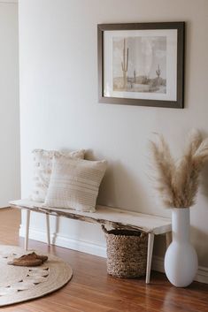 a white bench sitting in the middle of a room next to a vase and rug