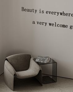 a chair sitting next to a glass table on top of a hard wood floor in front of a wall that says beauty is everywhere