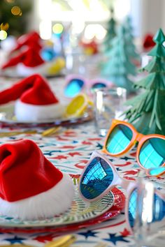 a table topped with plates and glasses covered in santa hats next to christmas tree decorations