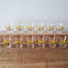 a row of shot glasses with yellow leaves on them sitting on a wooden counter top