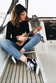 a woman sitting on the back of a boat while playing an ukulele guitar