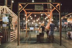 two people standing in front of a table with lights hanging from it's sides