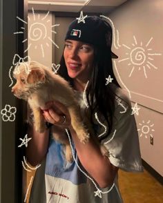 a woman is holding a small dog in her arms and smiling at the camera while wearing a baseball cap