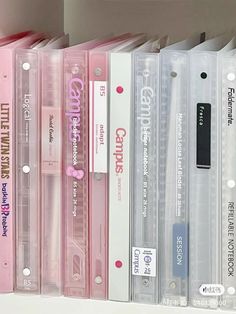 some pink and white binders are stacked on top of each other in a row