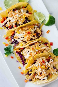 three tacos on a white plate with limes and cilantro