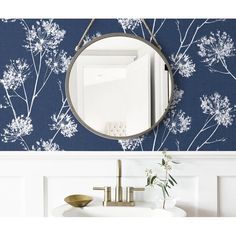 a mirror hanging on the side of a wall next to a sink and vase with flowers