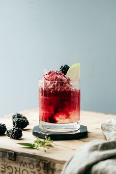 a red drink sitting on top of a wooden table next to blackberries and limes