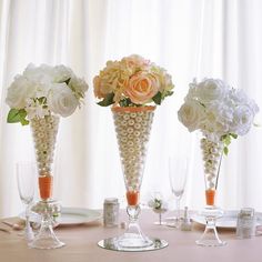 three vases filled with flowers on top of a table next to wine glasses and plates