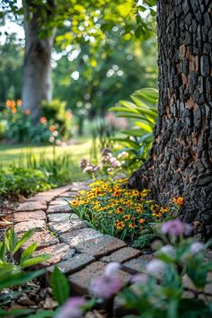 flowers are growing on the side of a brick path next to a tree and grass