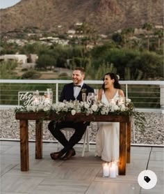 a bride and groom sitting at a table in front of a mountain with candles on it